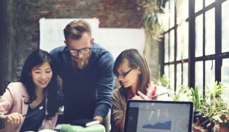 Three coworkers huddling over data analytics on computer screen