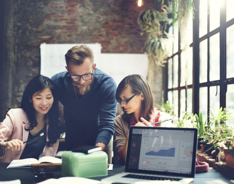 Three coworkers huddling over data analytics on computer screen