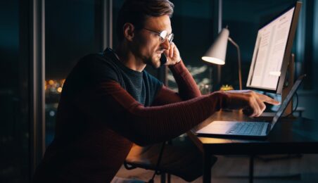 Emerging PE manager employee working after hours on two computer screens